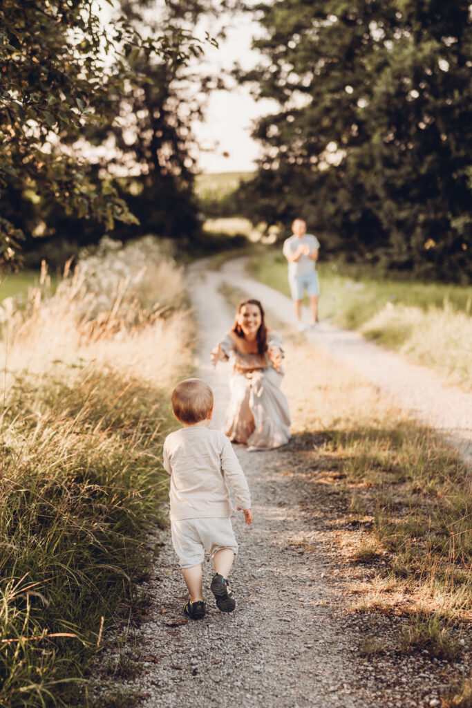 Auf dem Bild ist eine Mama zu sehen, die die Arme aufhält, um das ihr entgegenlaufende Kind aufzufangen. Das Kind läuft vom Betrachter weg auf die Mama zu.