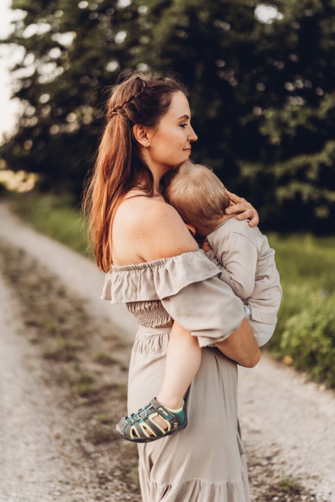 Eine Mama steht seitlich zur Kamera mit dem Kleinkind auf dem Arm, was den Kopf an ihre Brust lehnt.