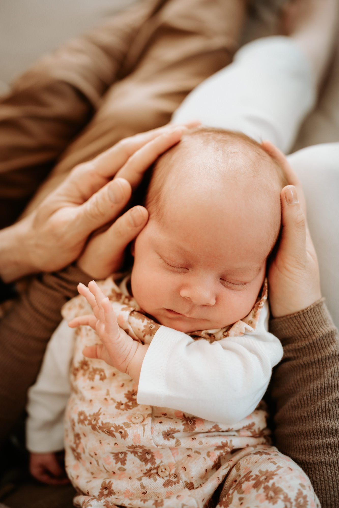 Das Bild zeigt ein schlafendes Neugeborenes im Arm seiner Eltern