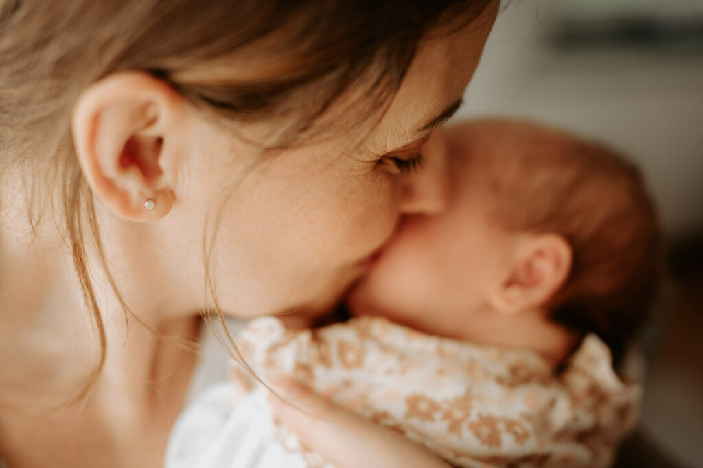 Das Bild zeigt eine Mama, die liebevoll ihr Gesicht an das ihres Neugeborenen kuschelt.