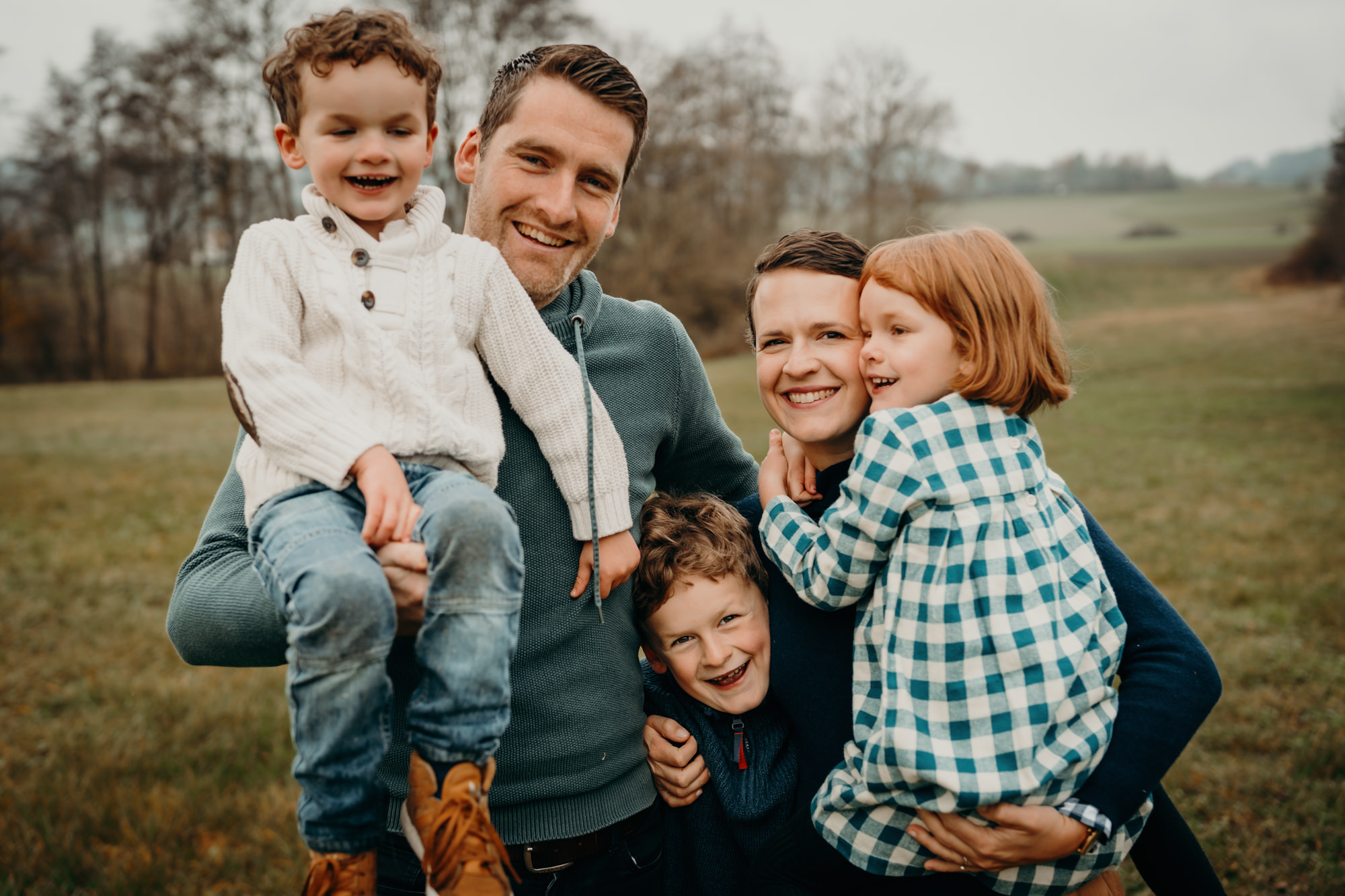 Das Bild zeigt eine Mama und einen Papa mit drei Kindern in der Natur. Sie lachen in die Kamera.