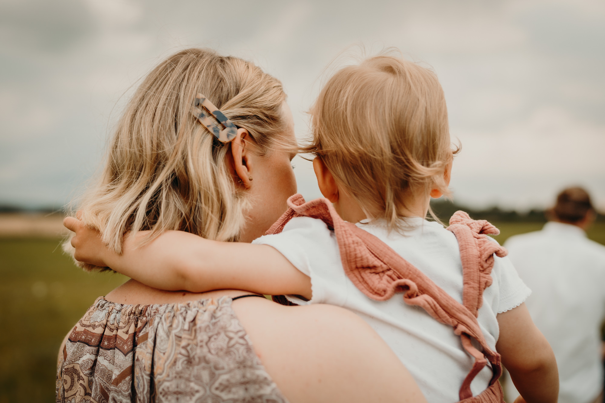 Das Bild zeigt eine Mama mit ihrer Tochter auf dem Arm. Die Tochter legt den Arm um den Hals der Mama.